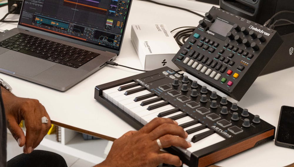 Producer’s hands playing an Arturia MiniLab MIDI controller next to a laptop running Ableton Live, with SoundID Reference box and Elektron Digitone synthesizer on the desk